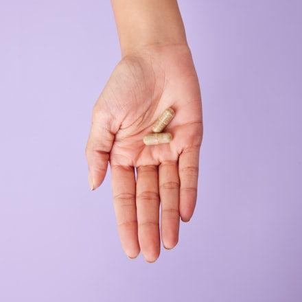 A person holding a supplement capsule in their palm outdoors